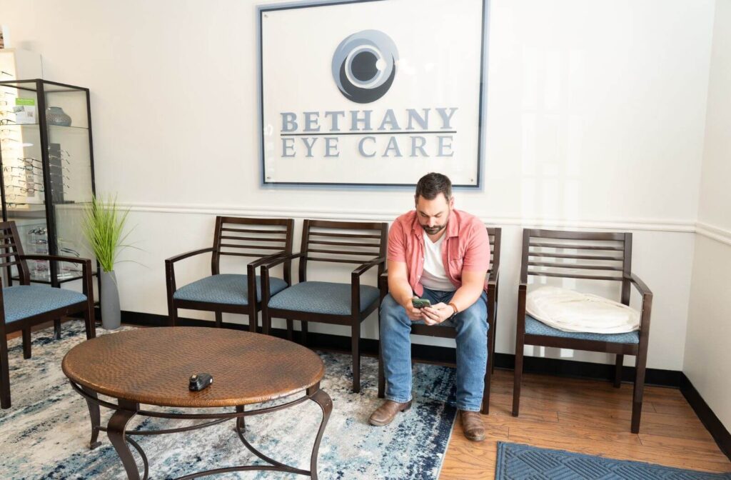 An adult sitting in the waiting area of Bethany Eye Care, looking at his phone