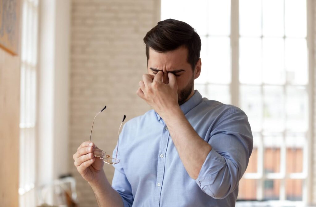 Person rubbing eyes while holding eyeglasses, showing eye strain or discomfort.