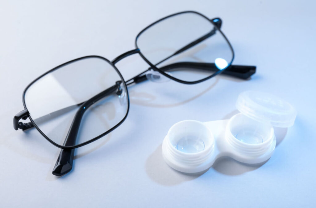 A pair of black eyeglasses and an open white contact lens case containing blue-tinted lenses, illustrating the differences between vision correction prescriptions.