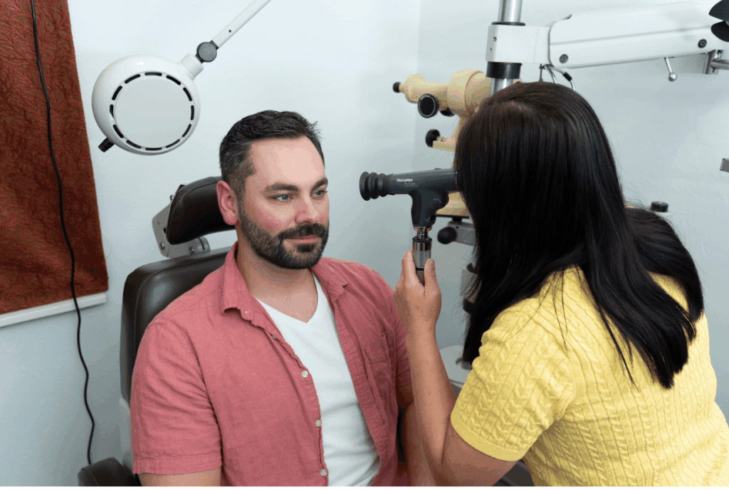 An eye care professional using a handheld ophthalmoscope to examine a patient's eye in a clinical setting.